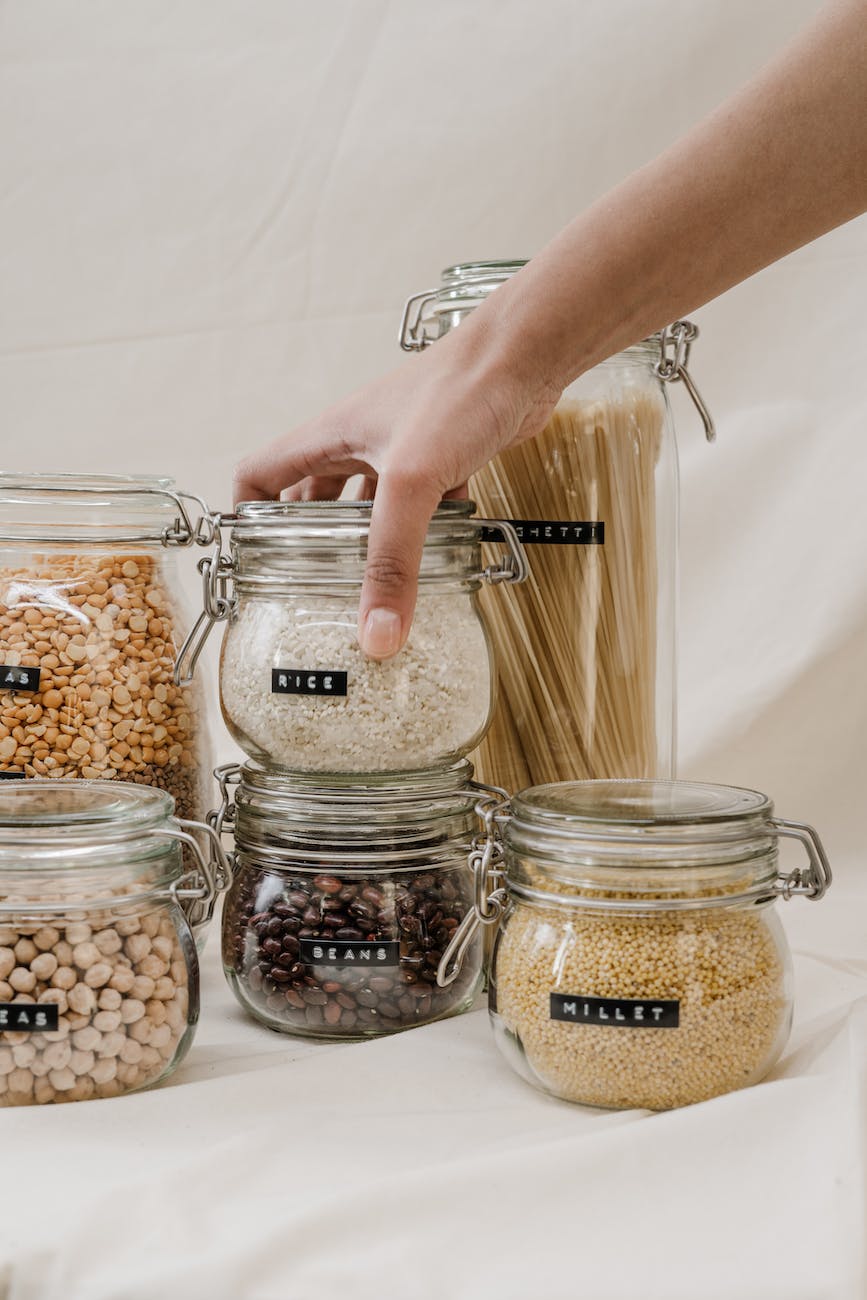 person holding clear glass jar with rice brown and white beans