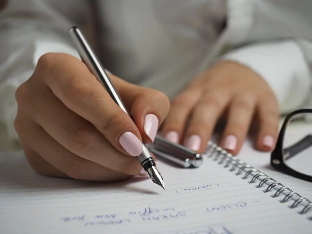 woman in white long sleeved shirt holding a pen writing on a paper