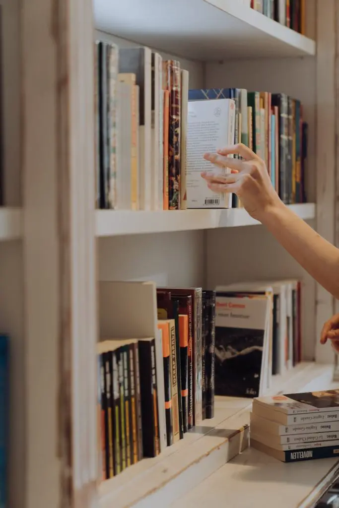 person holding white book in white wooden shelf